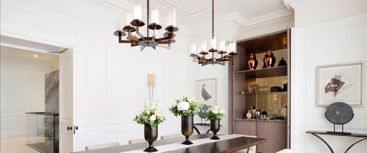 Bespoke bronze chandeliers over a dining table with a lit display alcove at Connaught Place